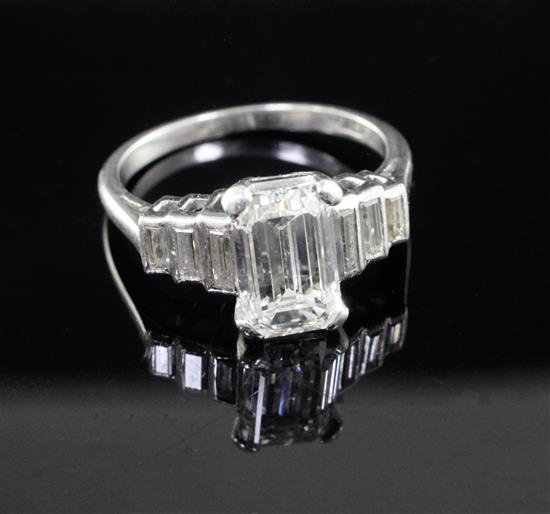 A 1930s/1940s Art Deco platinum and single stone emerald cut diamond ring, with graduated baguette cut diamond set shoulders,